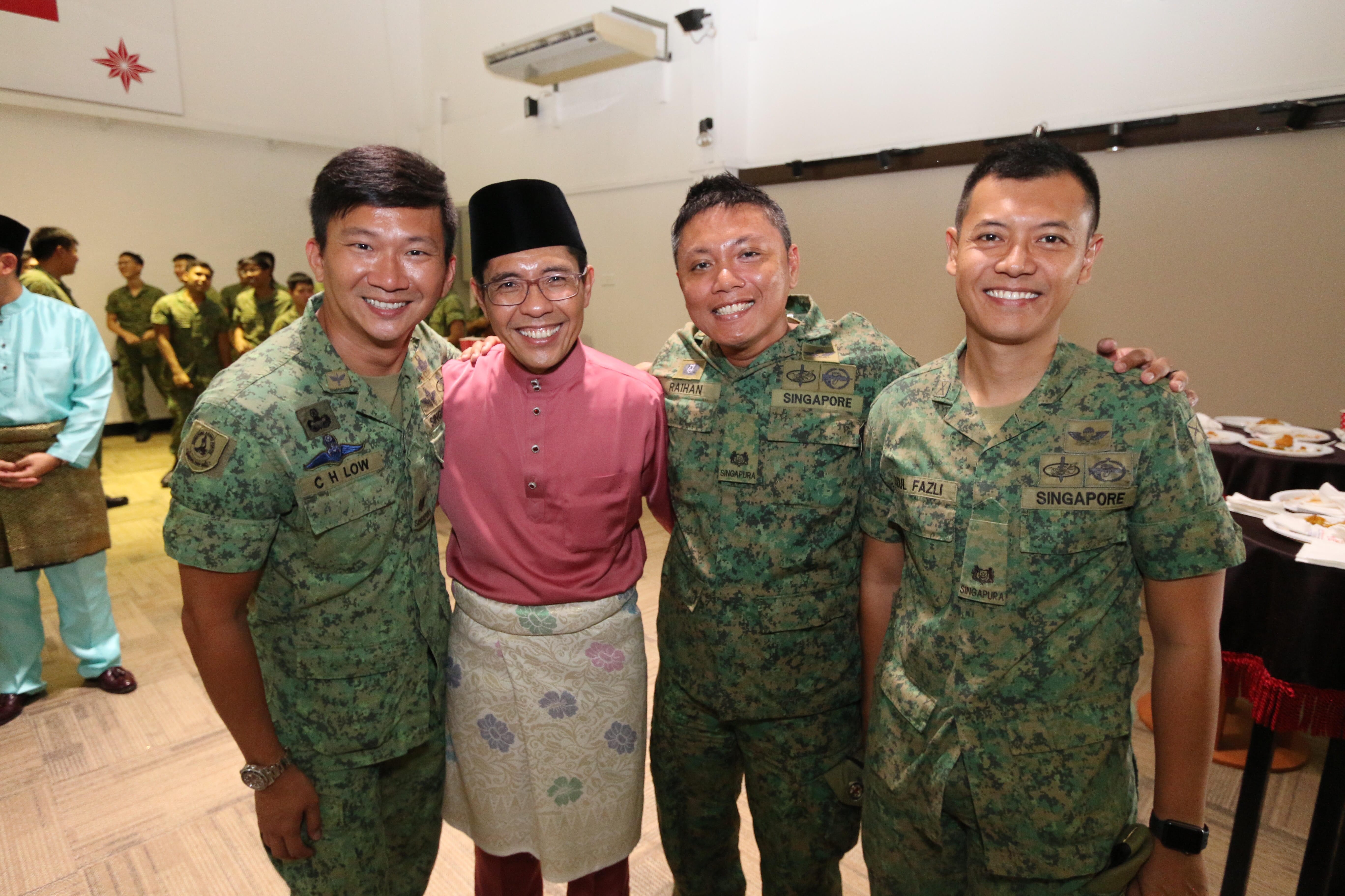 Four men pose together; three in Singapore military uniforms and one in traditional Malay clothing.